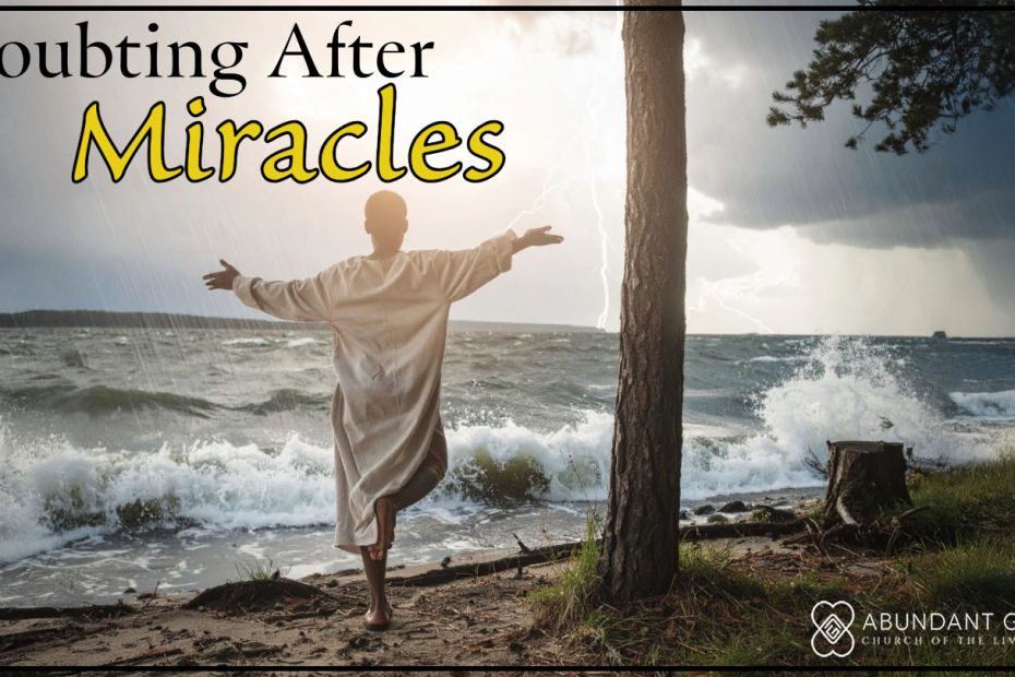 A man with his arms extended in the air to his side, standing by a lake with a storm in the background.