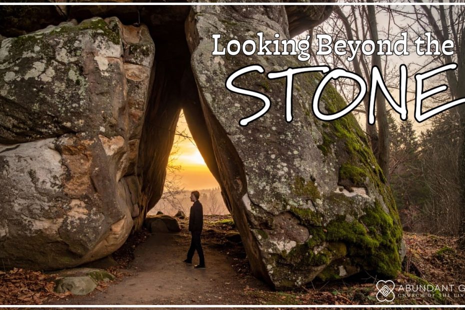 A person standing in the woods, gazing at a massive stone that blocks the entrance of a cave.